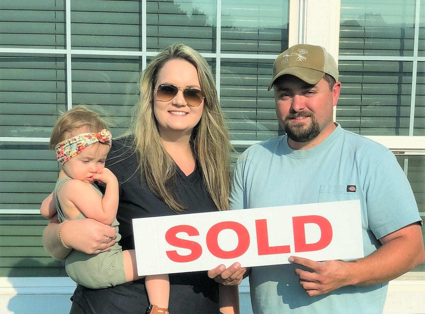 A couple holding a sold sign with their child.