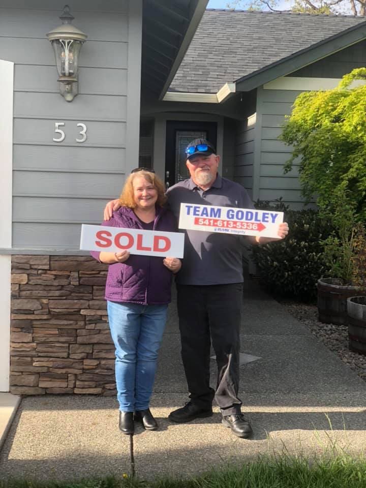 A couple holding up sold signs in front of their home.
